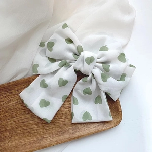 Detail of white satin bow with green hearts on a decorative wooden tray background