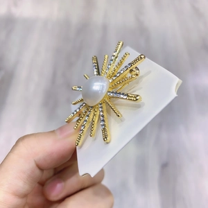 Golden starburst brooch with central faux pearl and glittering rhinestone accents