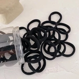 Détail d'élastiques à cheveux noirs sans couture rangés dans un pot cylindrique clair