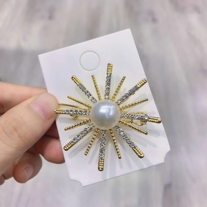 Golden sunburst star brooch with centered pearl and sparkling crystal accents on card