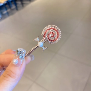 Détail d'une pince à cheveux sucette dorée avec des strass rouges et une perle blanche