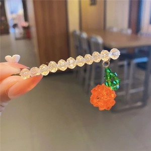 Close-up of beaded hair clip with transparent faceted crystals and orange fruit pendant
