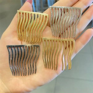 Set of four wavy metal hair combs in gold, silver and black finishes held in hand