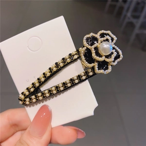 Dettaglio di un fermaglio per capelli a camelia con perle bianche e strass neri brillanti