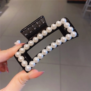 Close-up of a large black acrylic hair claw clip decorated with elegant double-row pearls