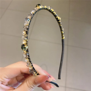 Détail du serre-tête noir vintage avec fil doré et cristaux verts et transparents