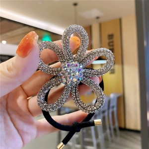 Handheld view of a sparkling floral hair tie with silver rhinestones and black elastic band