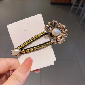 Detail of vintage gold chain hair clip featuring a metal daisy and large pearl inlay
