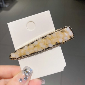 Détail d'une pince à cheveux dorée avec pierres en résine crème et chaîne perlée