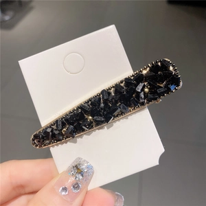 Détail d'une barrette dorée ornée de cristaux noirs et strass tenue à la main