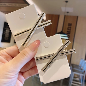 Dettaglio di fermagli coreani a X con perle e strass su un supporto di cartone bianco