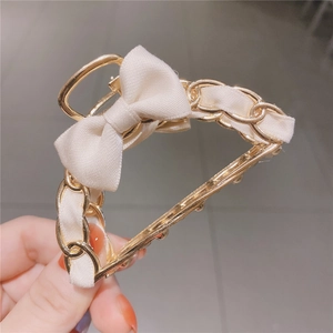 Detail of elegant cream satin bow hair claw clip with golden metal chain weave