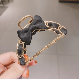 Close-up of golden metal chain hair claw with black ribbon and elegant bow detail