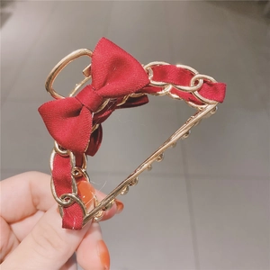 Detail of elegant gold metal chain hair claw with red ribbon and bow tie decoration