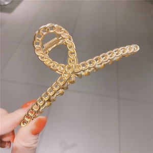 Pince à cheveux élégante en métal doré avec design de chaîne tenue sur fond gris