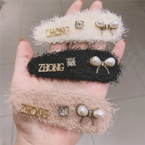 Three plush hair clips with ZHONG letters, rhinestones and pearls held in hand