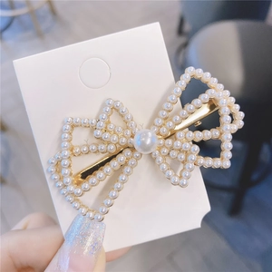 Détail d'une pince à cheveux avec nœud creux et perles blanches sur base en métal doré