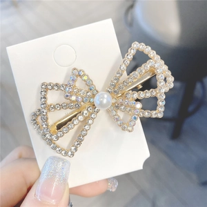 Gros plan sur pince à cheveux nœud doré avec strass blancs et perle centrale