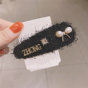 Detail of tweed hair clip with pearl bow, crystal stone, and golden metal lettering