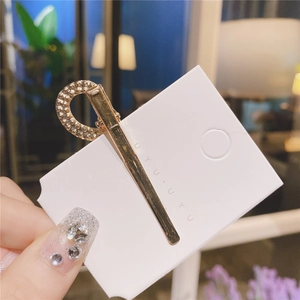 Gros plan d'une pince à cheveux dorée en forme de U avec strass sur carte support