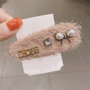 Detail of pink plush hair clip with golden letters, rhinestone, and pearl bow decoration