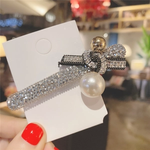 Détail d'une pince à cheveux de luxe avec nœud strass, boule dorée et perle nacrée
