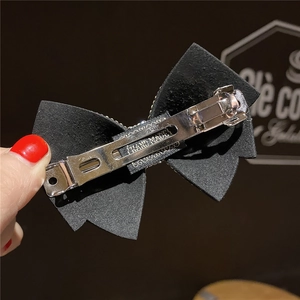 Detailed view of black rhinestone bow hair clip with silver metal spring mechanism