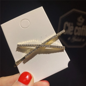 Détail d'une barrette dorée en X ornée de cristaux blancs sur sa carte de support