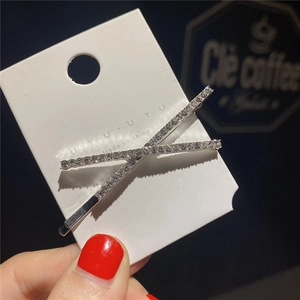 Vue détaillée d'une barrette en X en métal argenté avec strass brillants sur carton