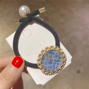 Close-up of black elastic hair tie with blue tweed round pendant and white pearl detail
