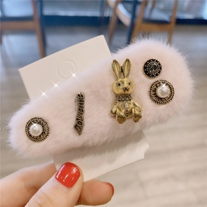 Détail d'une pince à cheveux rose en peluche avec lapin doré, lettrage Loveme et perles