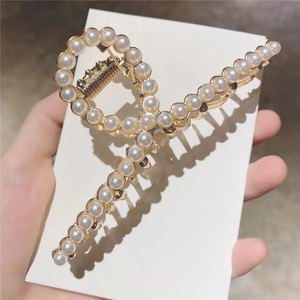 Détail d'une pince à cheveux dorée avec design croisé et perles blanches incrustées