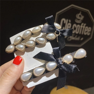 Elegant black satin bow hair clips with pearls on display card in a warm cafe setting