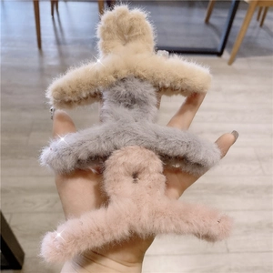 Close-up of three plush faux fur hair claws in beige, grey, and pink colors