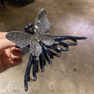 Détail d'une grande pince à cheveux papillon ornée de strass brillants tenue à la main