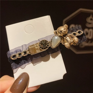 Détail d'une pince à cheveux vintage avec ours doré, strass et dentelle en maille noire