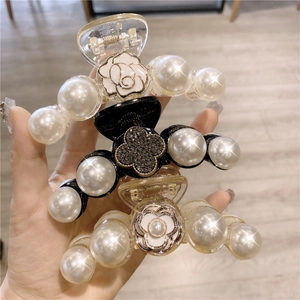 Détail de trois pinces à cheveux en perles avec camélia et trèfle tenues en main