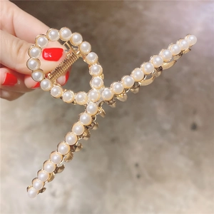 Détail d'une pince à cheveux dorée ornée de deux rangées de perles blanches lustrées