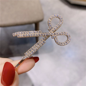 Gros plan d'une pince à cheveux dorée en forme de ciseaux avec strass incrustés
