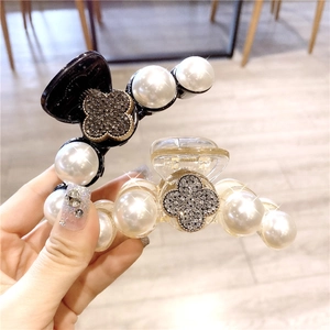 Détail de pinces à cheveux camélia et perles avec breloques trèfle en noir et champagne