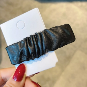 Detail der schwarzen gefalteten Kunstleder-Textur dieser minimalistischen Haarspange für Damen