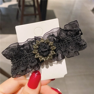 Detailed view of a black lace hair clip with gray rhinestone ornament on display card