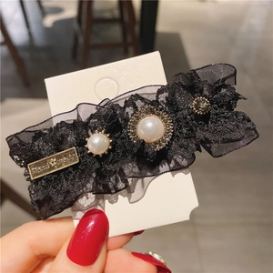 Detail of handmade black lace hair clip featuring pearls, rhinestones and vintage metal tag