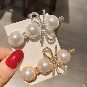 Détail de pinces à cheveux avec nœud en strass et perles blanches sur base dorée