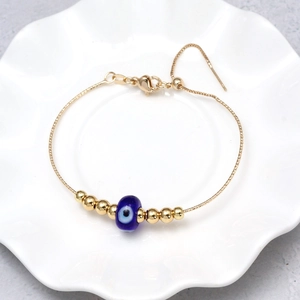 Close-up of golden box chain Evil Eye bracelet on a white wavy ceramic jewelry dish
