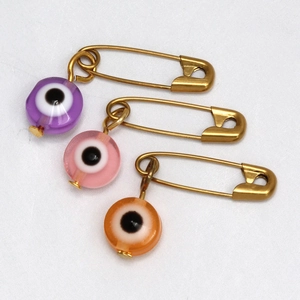 Detalle de imperdibles de ojo turco en violeta rosa y naranja con acabado dorado
