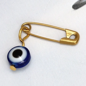Primer plano de un alfiler de acero dorado con cuenta de ojo azul sobre tela
