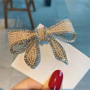 Détail d'une pince à cheveux nœud doré avec perles blanches et strass brillants