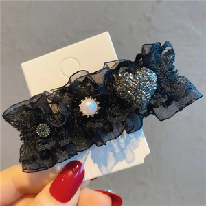 Detail of vintage black lace hair clip with pearls, green gemstone, and rhinestone heart