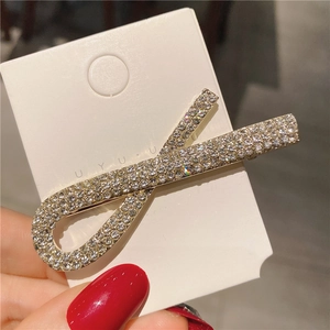 Détail d'une pince à cheveux dorée en forme de X ornée de strass brillants pavés